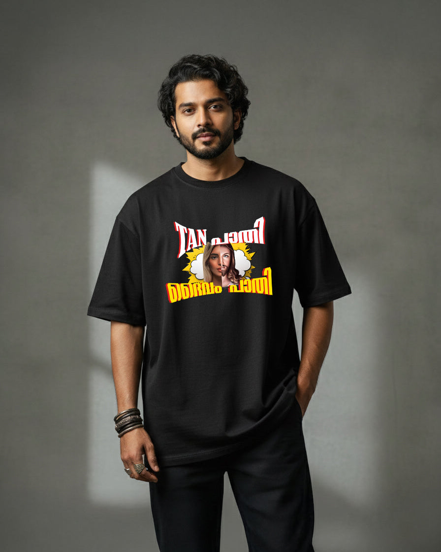 A man with wavy dark hair and a beard stands against a gray background, wearing the "Tan Pathi Deivam Pathi" premium bio-washed oversized t-shirt (220 GSM cotton) with a graphic print of a woman's face and colorful stylized text.
